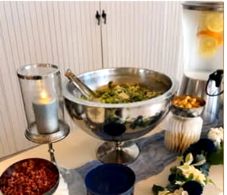 A silver salad bowl and infused water dispenser on a styled buffet table.
